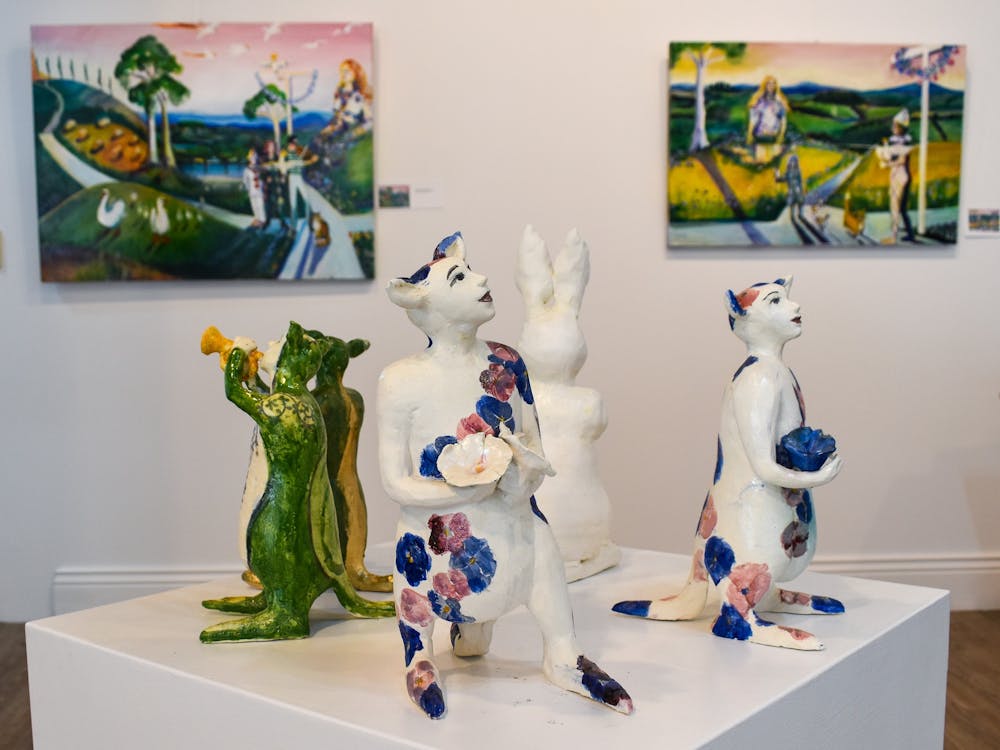 Landscape paintings in the background with whimsical ceramic characters on a plinth in the front.