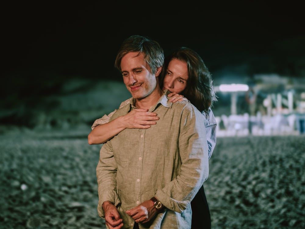 Two people standing on a beach, one hugging the other from behind