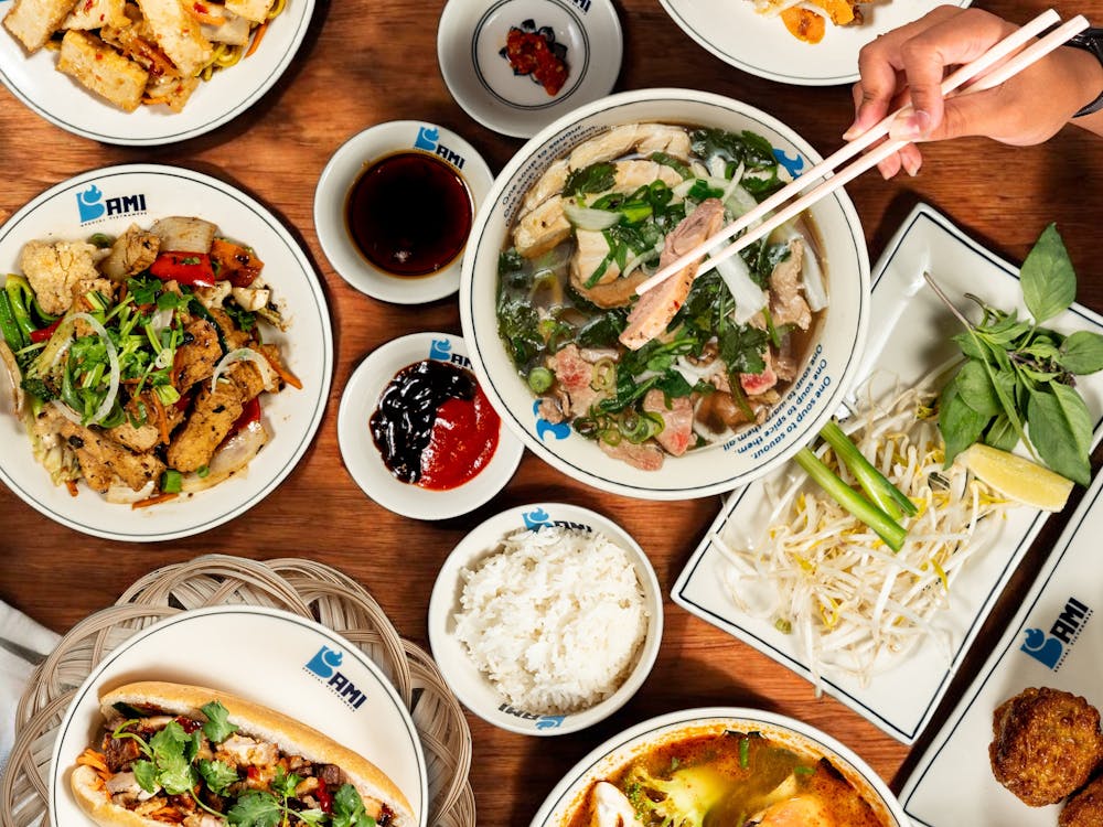Overhead flatlay of Bami Vietnamese dishes on a timber table including pho broth with chopsticks