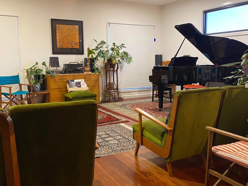 A black grand piano sits in front of lounge chairs; colourful rugs are on wooden floorboards.