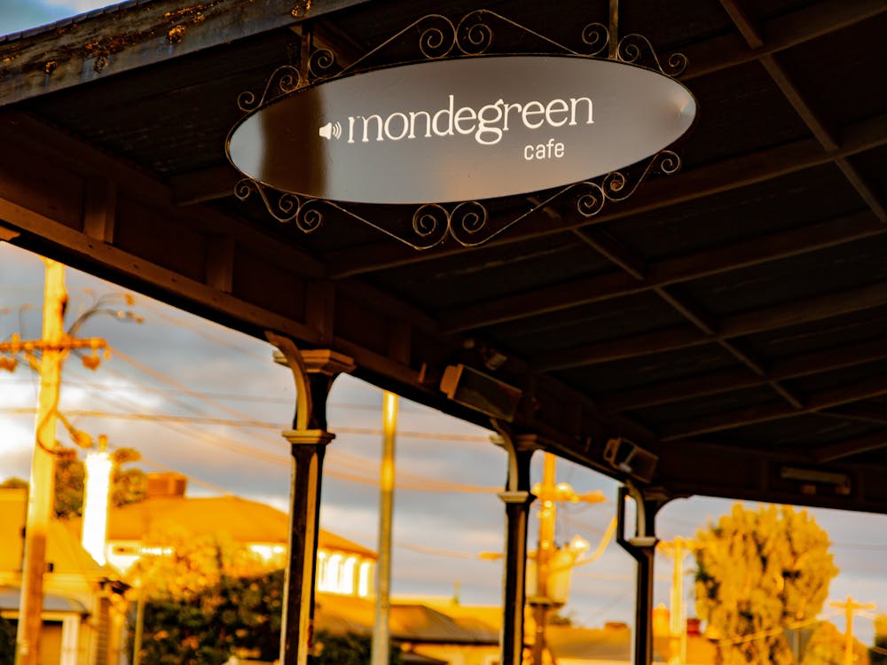 Oval sign of Mondegreen Cafe's logo under the front veranda.