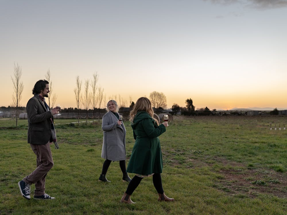 Three people walking holding wine glasses in a winery at sunset