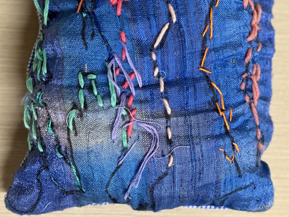 A blue fabric cushion with coloured stitching on the cover.