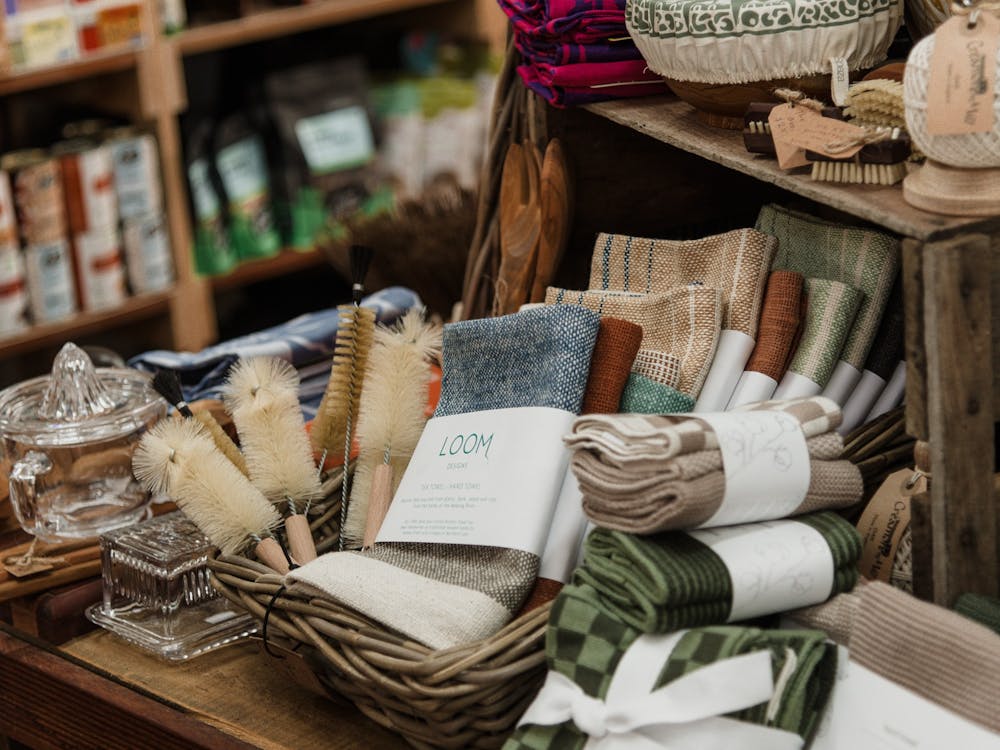 A basket full of hand woven cloths and cleaning bottle brushes on a shelf with glass butter dish