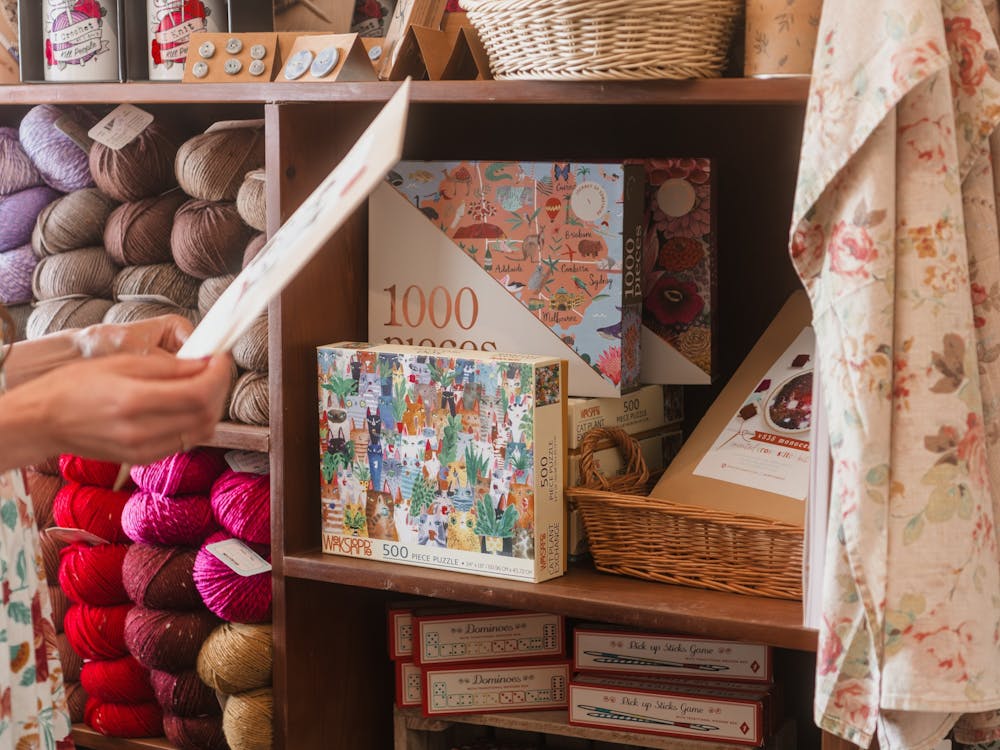 person holding a book near a shelf full of wool yarn and puzzles