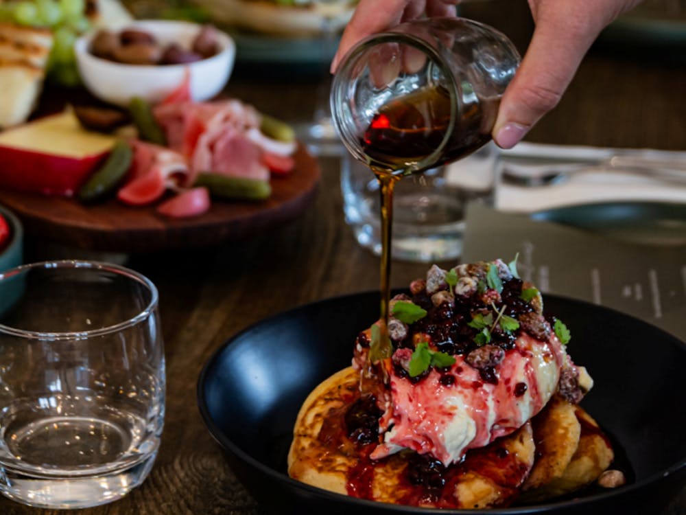 Maple syrup poured over pancakes topped with berries and mascarpone cream.