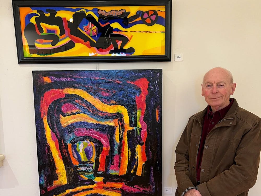 Russell is pictured with 2 of his dynamic, colorful abstract acrylic paintings.