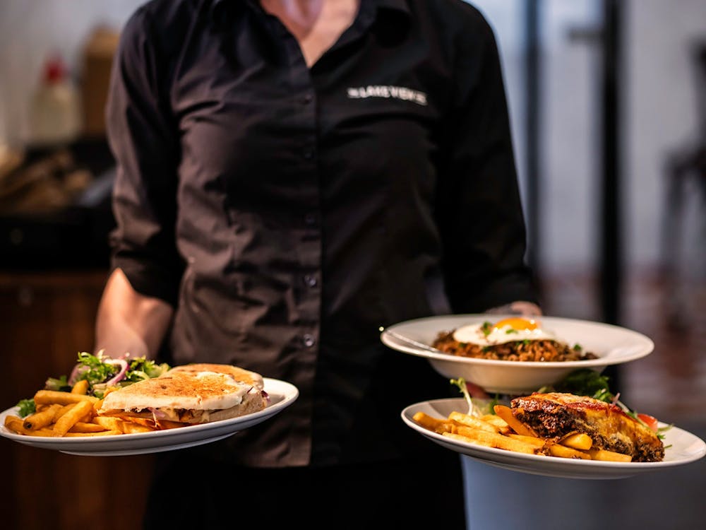 Staff member carrying three freshly prepared meals through the restaurant.