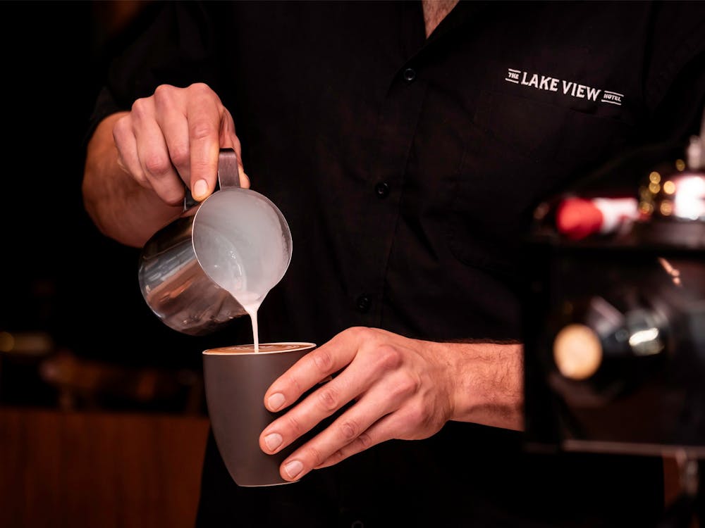 Barista pouring steamed milk into a freshly brewed coffee.