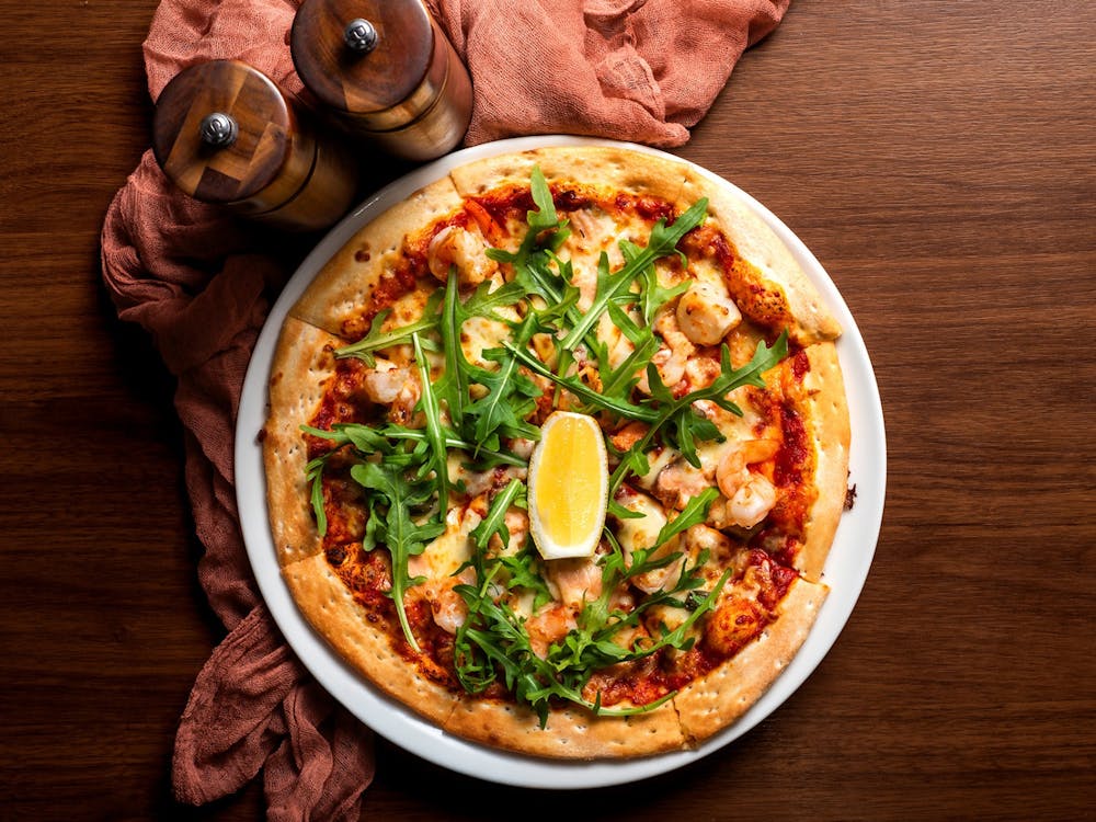Seafood pizza topped with prawns, salmon, rocket and lemon on a wooden table.