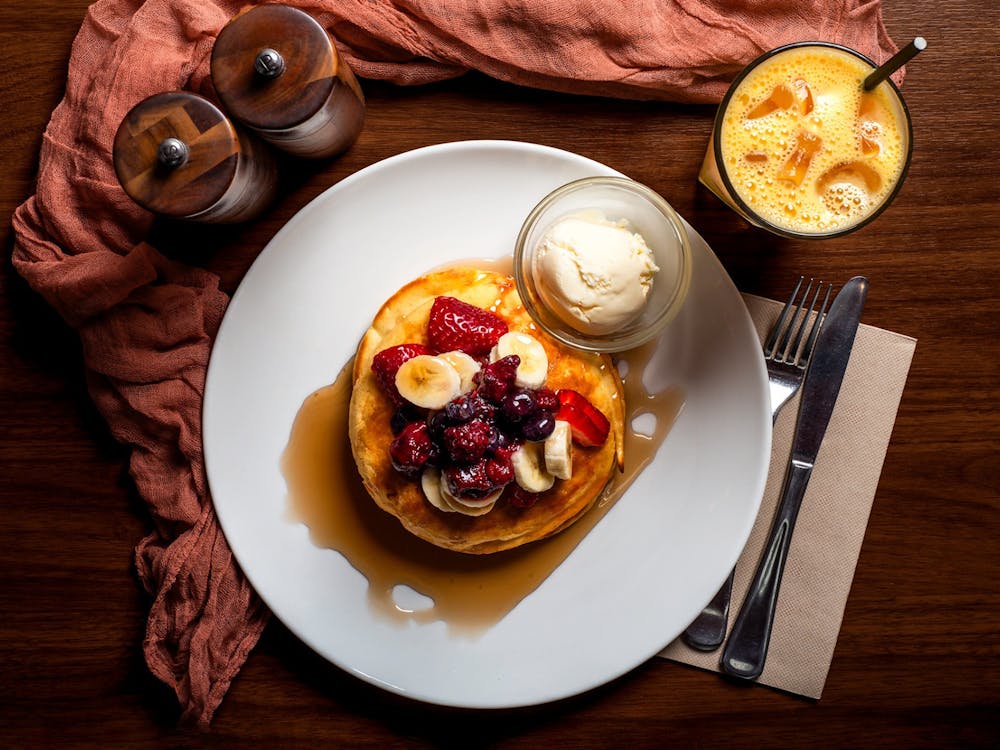 Stack of pancakes topped with fresh berries, banana, maple syrup and ice cream, served with juice,