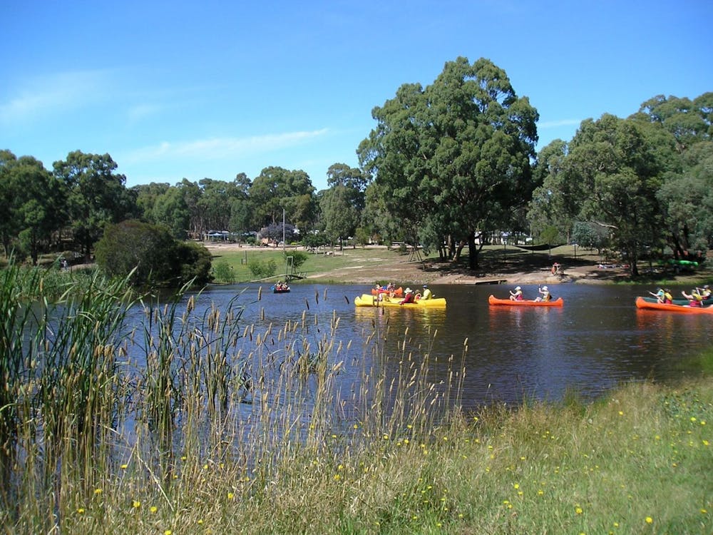A peaceful dam with three canoes being paddled by school children