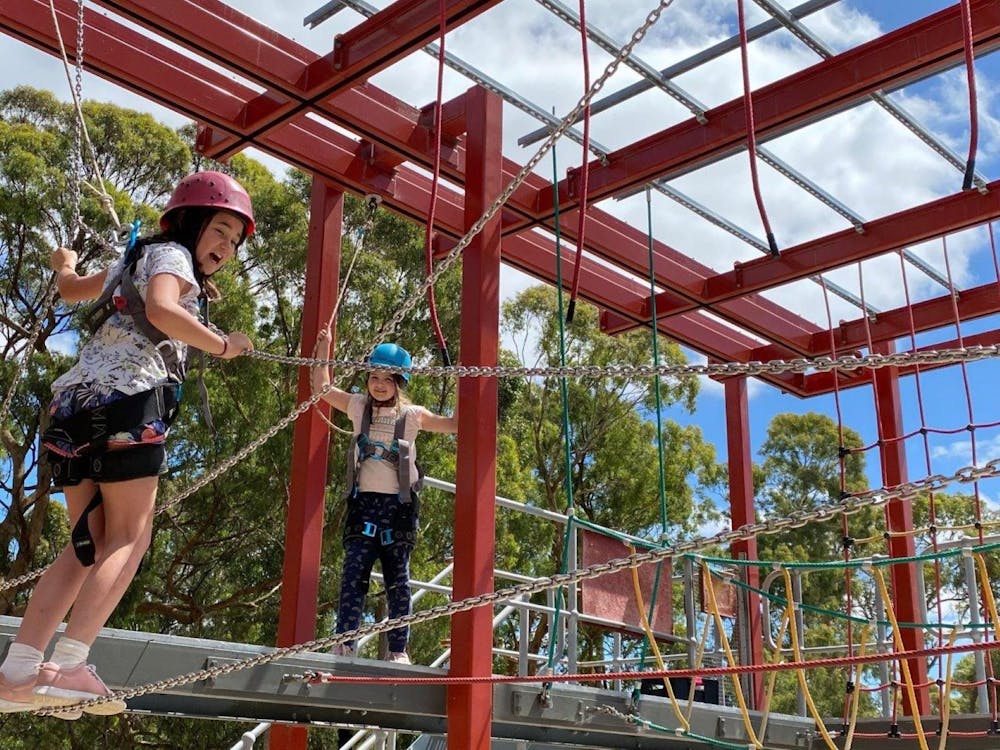 Two school aged girls navigating a clip and climb and laughing