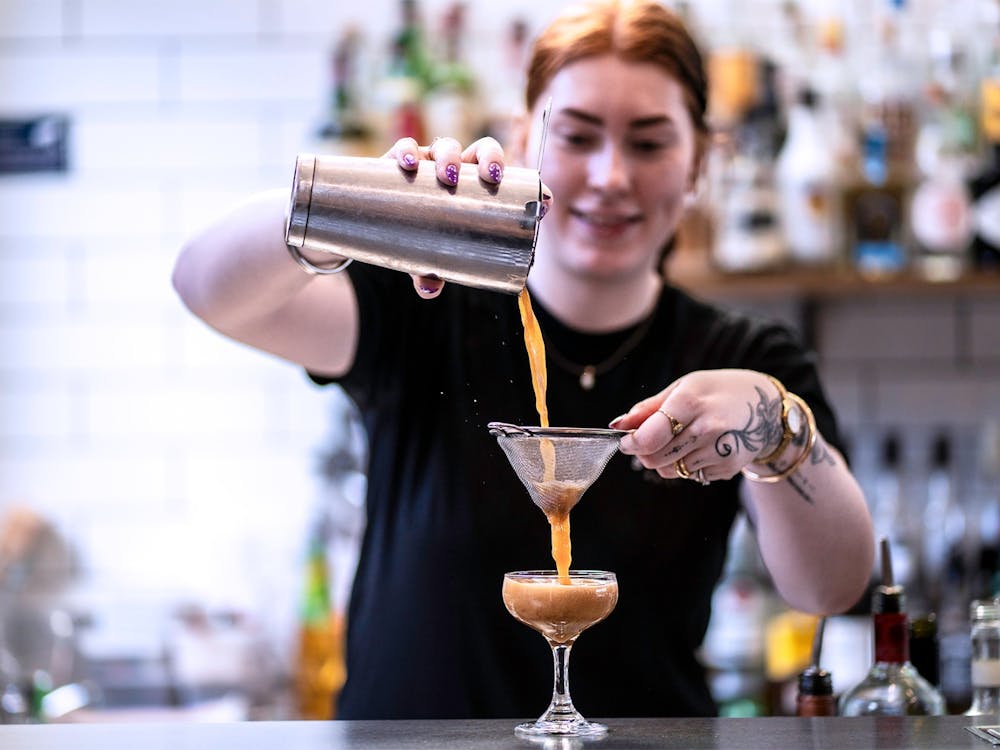 Bartender straining a freshly made cocktail into a coupe glass behind the bar at The North Star