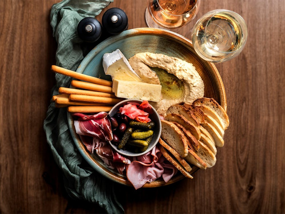 Share platter with cheeses, cured meats, hummus, pickles, bread and crackers, served with wine