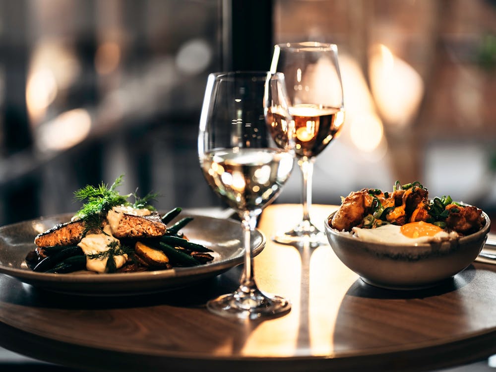 Dining table with a salmon dish, a chicken rice bowl and glasses of wine inside The North Star Hotel