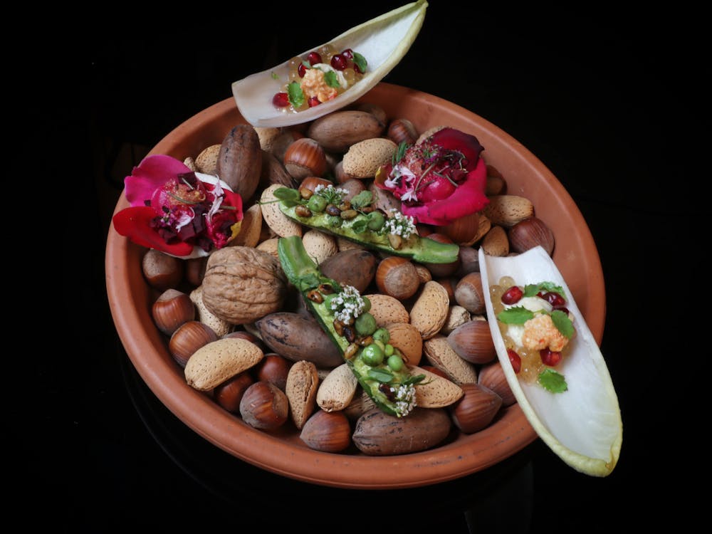 A terracotta dish filled with assorted nuts and topped with colourful bite-sized degustation dishes