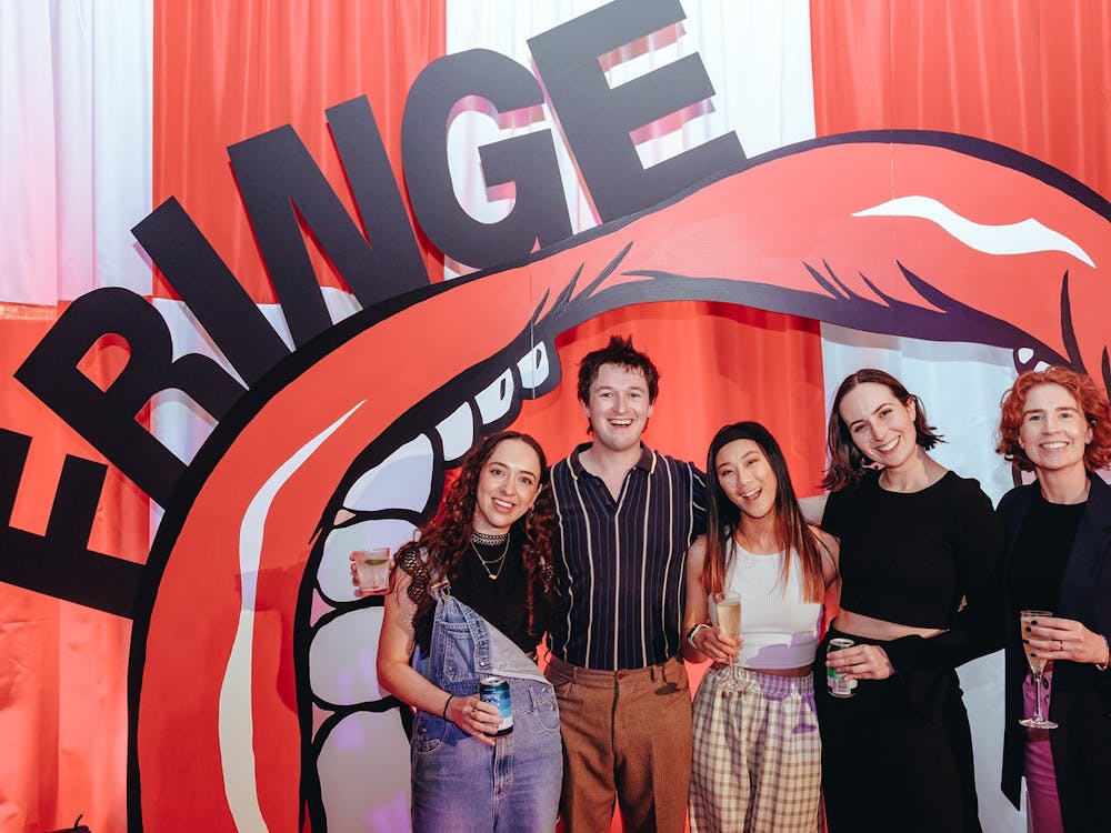 Six people smile and pose together at an event in front of a large red-and-white inflatable mouth an
