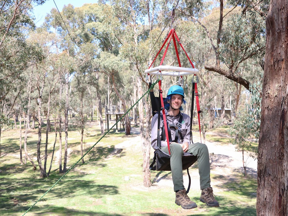 A camper uses an adaptive suspended harness on a zipline