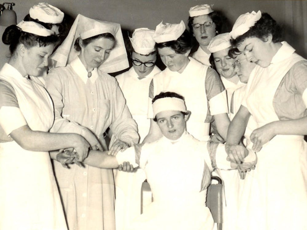 Black and white photo of nurses practicing bandages on one another - July 1958