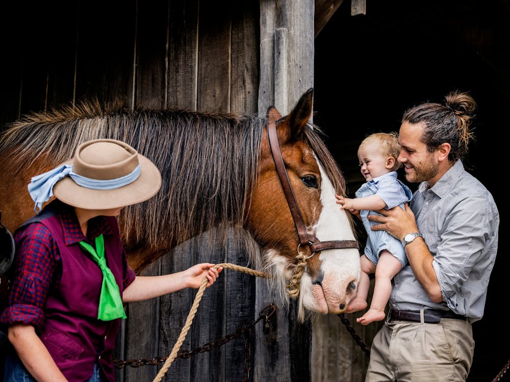 Man holding baby reaching out to a horse with an animal handler
