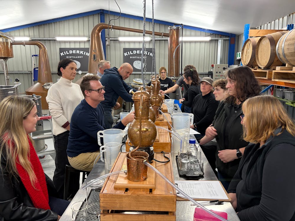 Ten adults sitting at bench with small stills distilling gin