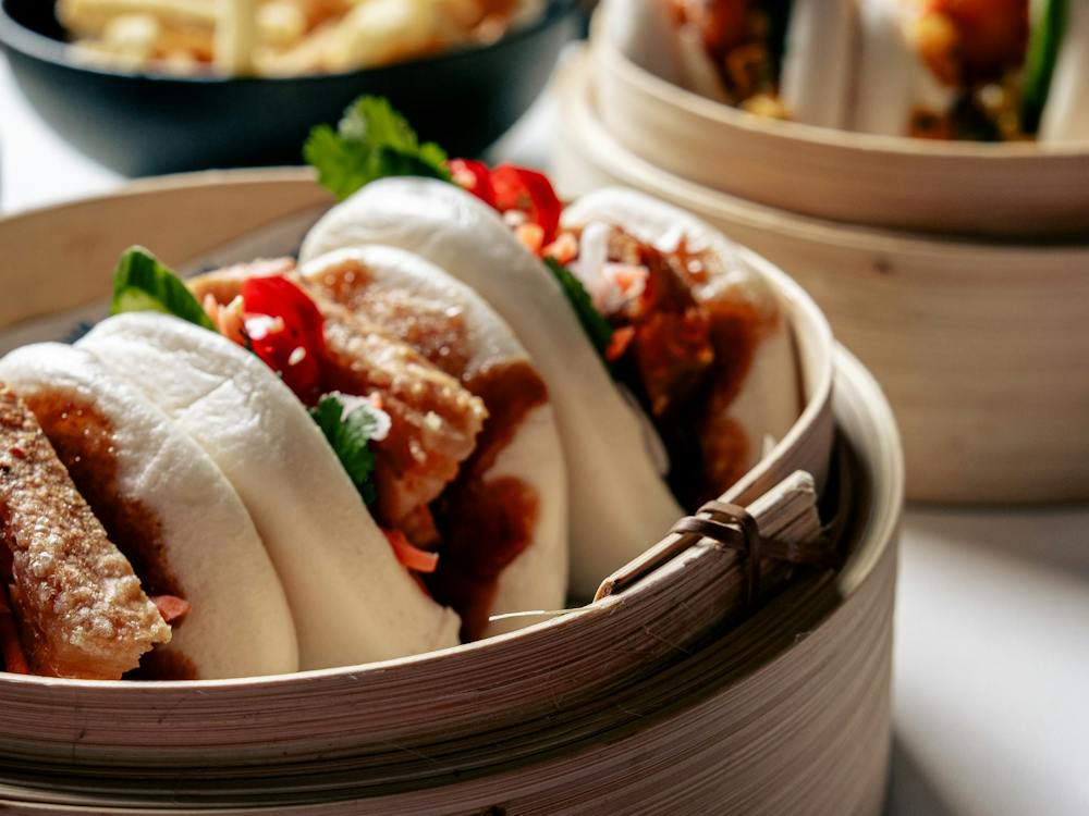 Fresh bao buns served in a bamboo steamer with chilli and coriander.