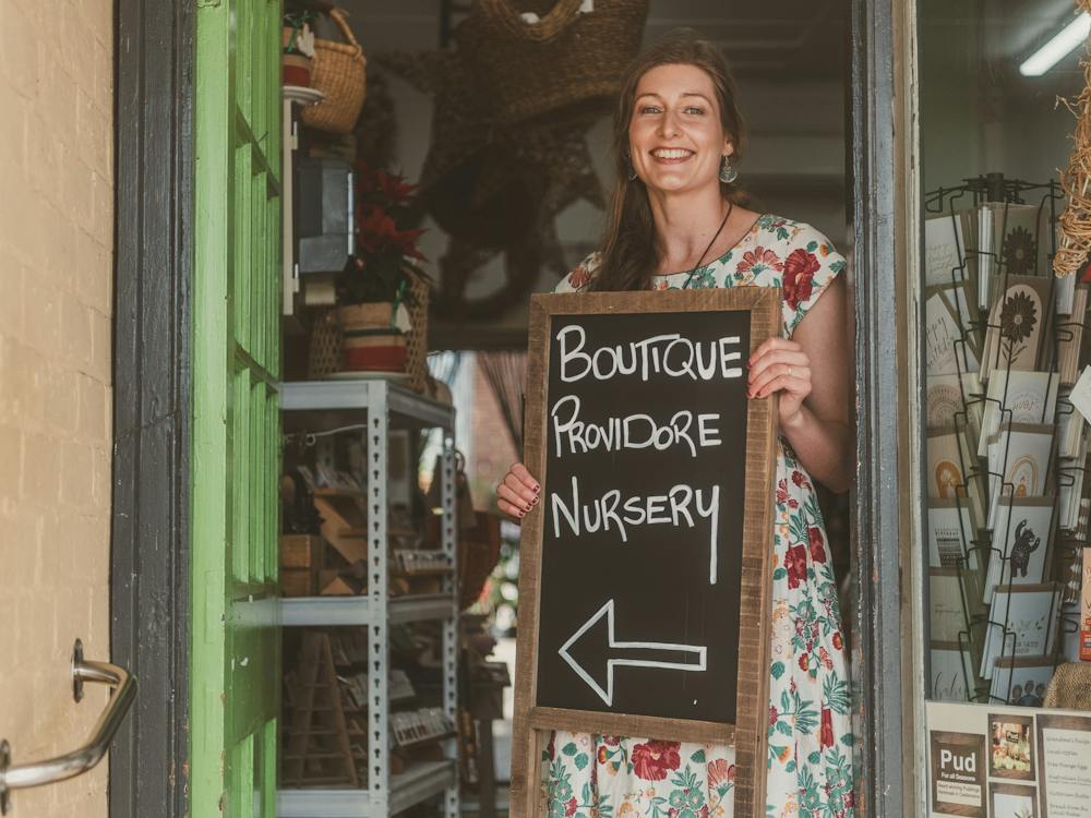 woman holding sign that says, boutique, providore, nursery