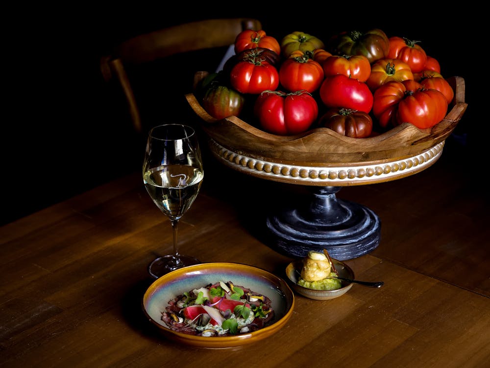 Plated dish and glass of wine placed next to a bowl of tomatoes