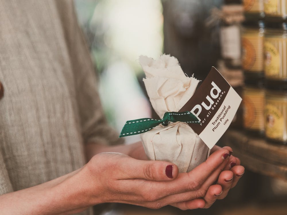 A pair of hands holds a small wrapped Christmas pudding.